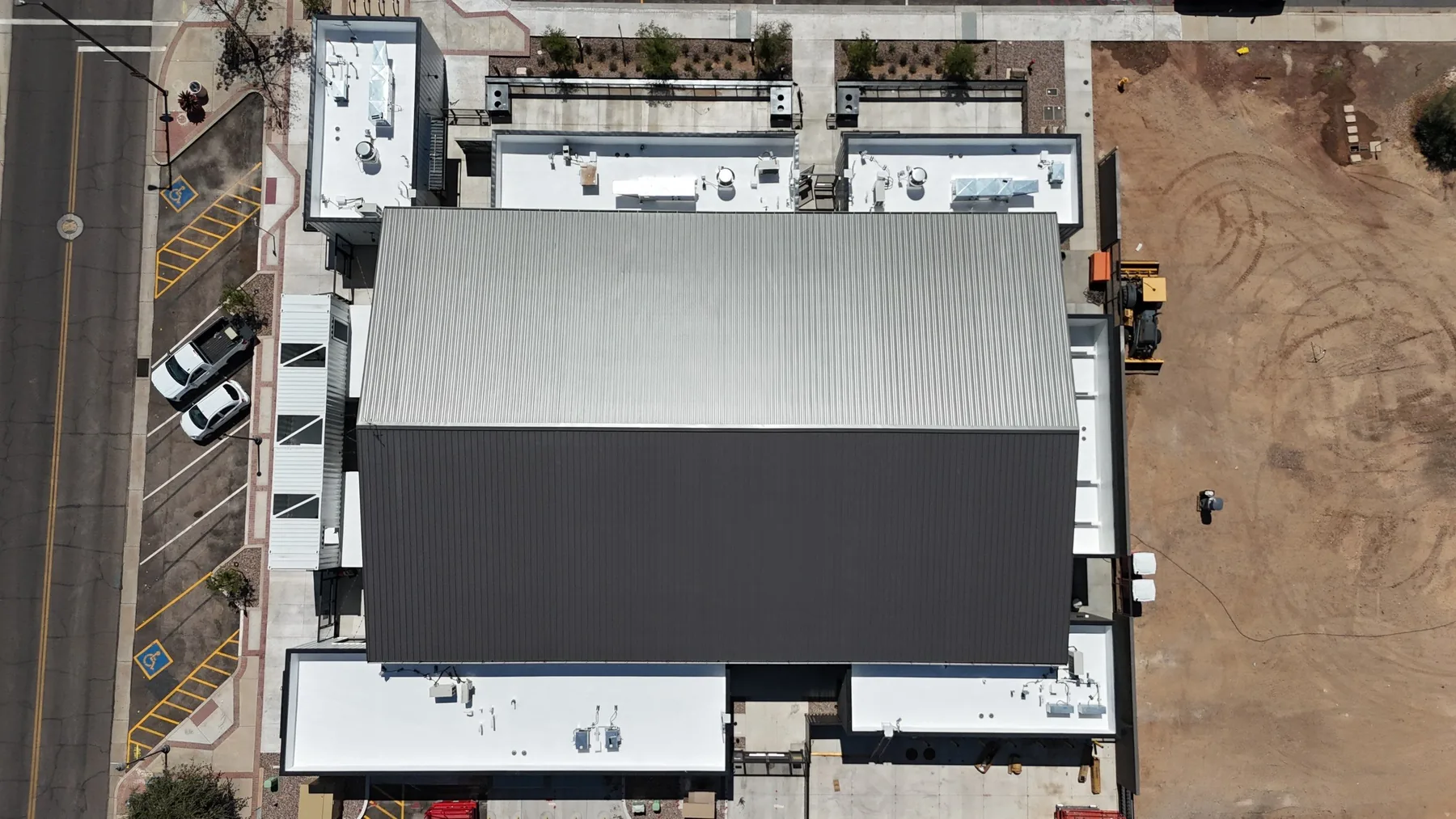 Top-down aerial view of gray standing-seam metal and dark low-slope roofing with white perimeter sections