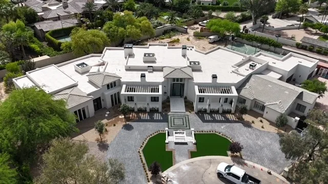 Oblique aerial view of white low-slope roofing and gray tiled wings above a curved driveway