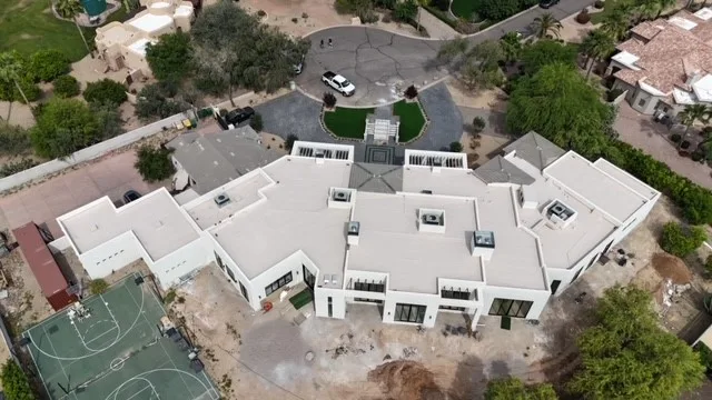 High aerial view of white low-slope roofing with small gray tiled sections and angular footprint