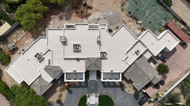 Near-vertical aerial view of white low-slope roofs and gray tiled wings beside a tennis court