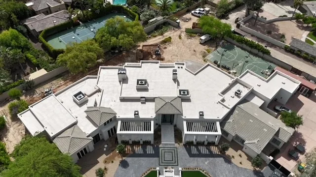 Oblique aerial view of expansive white low-slope roofing with gray tiled entrances and rooftop units