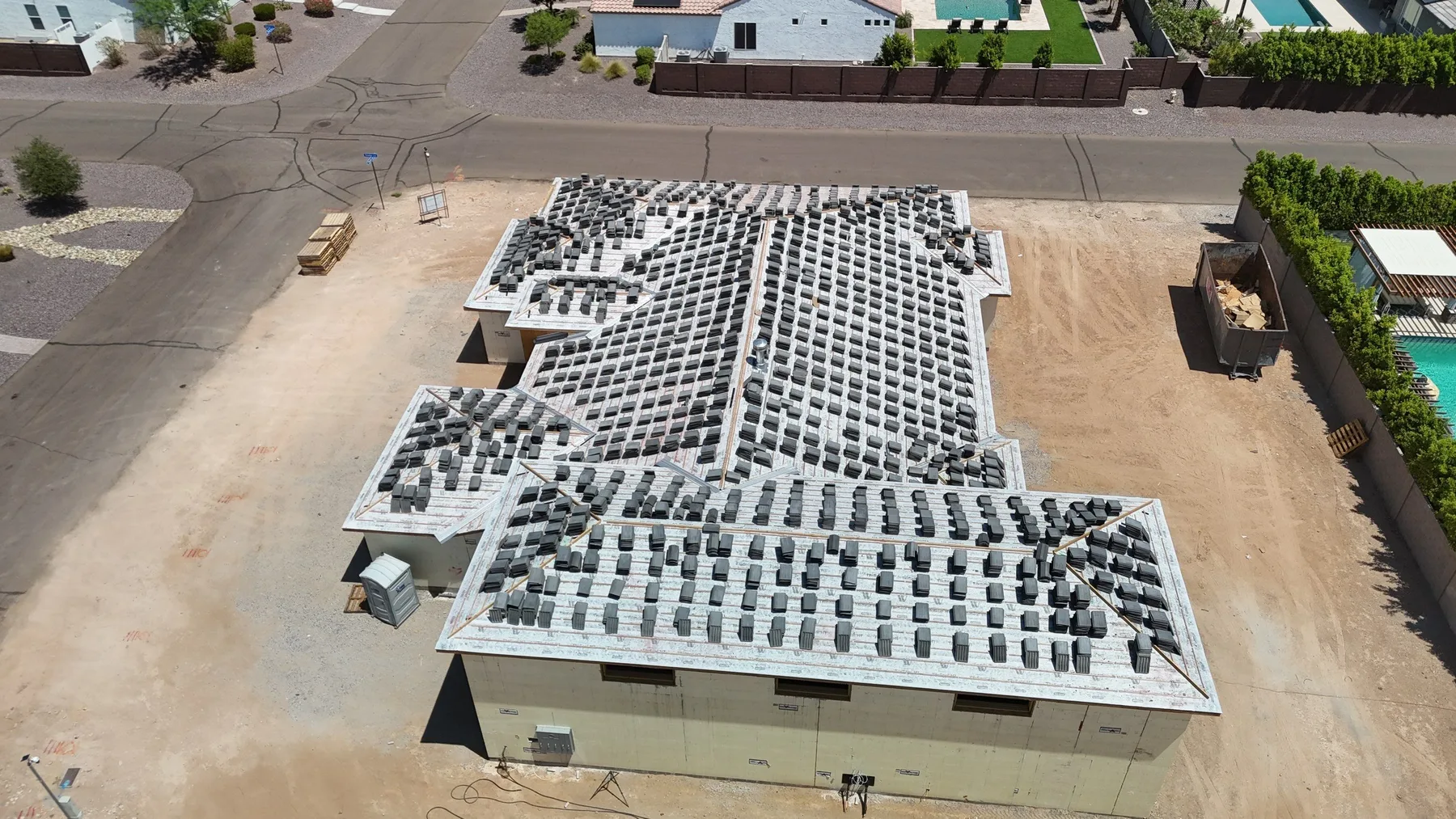 Overhead aerial view of gray underlayment with staged dark tiles on a sprawling pitched roof