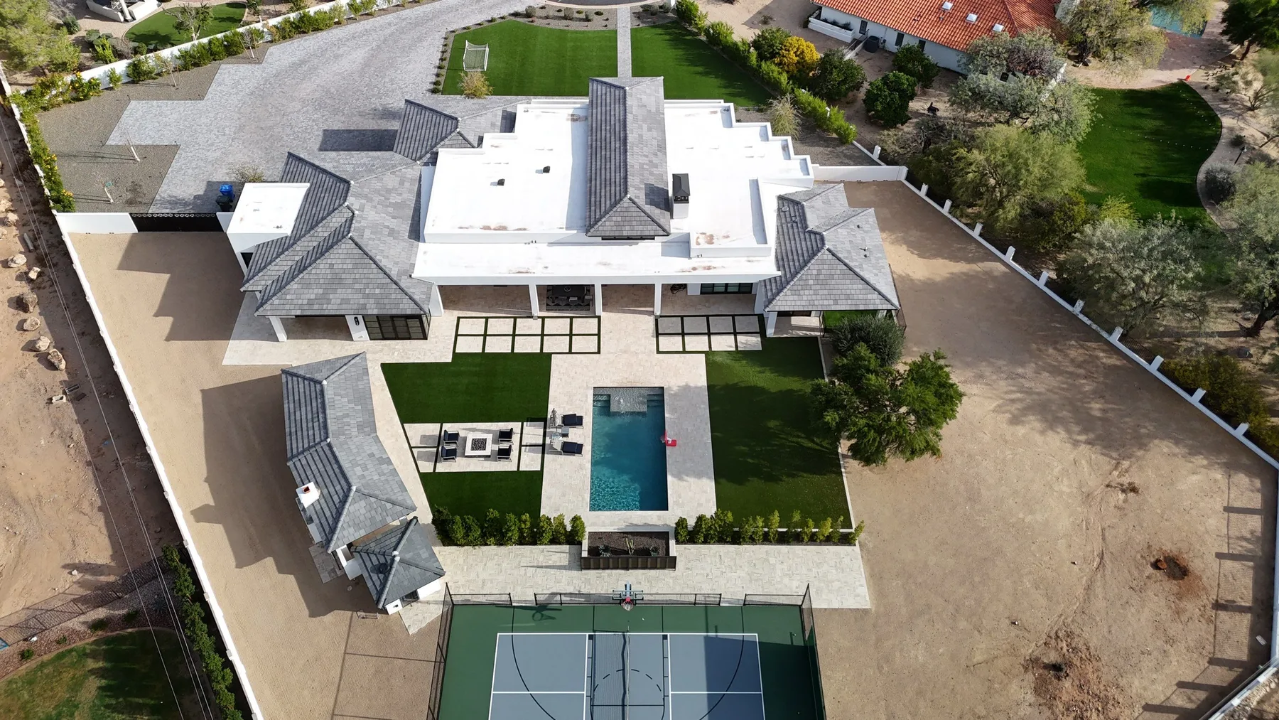 Oblique aerial view of white flat roofing and dark gray tiled hips beside a swimming pool
