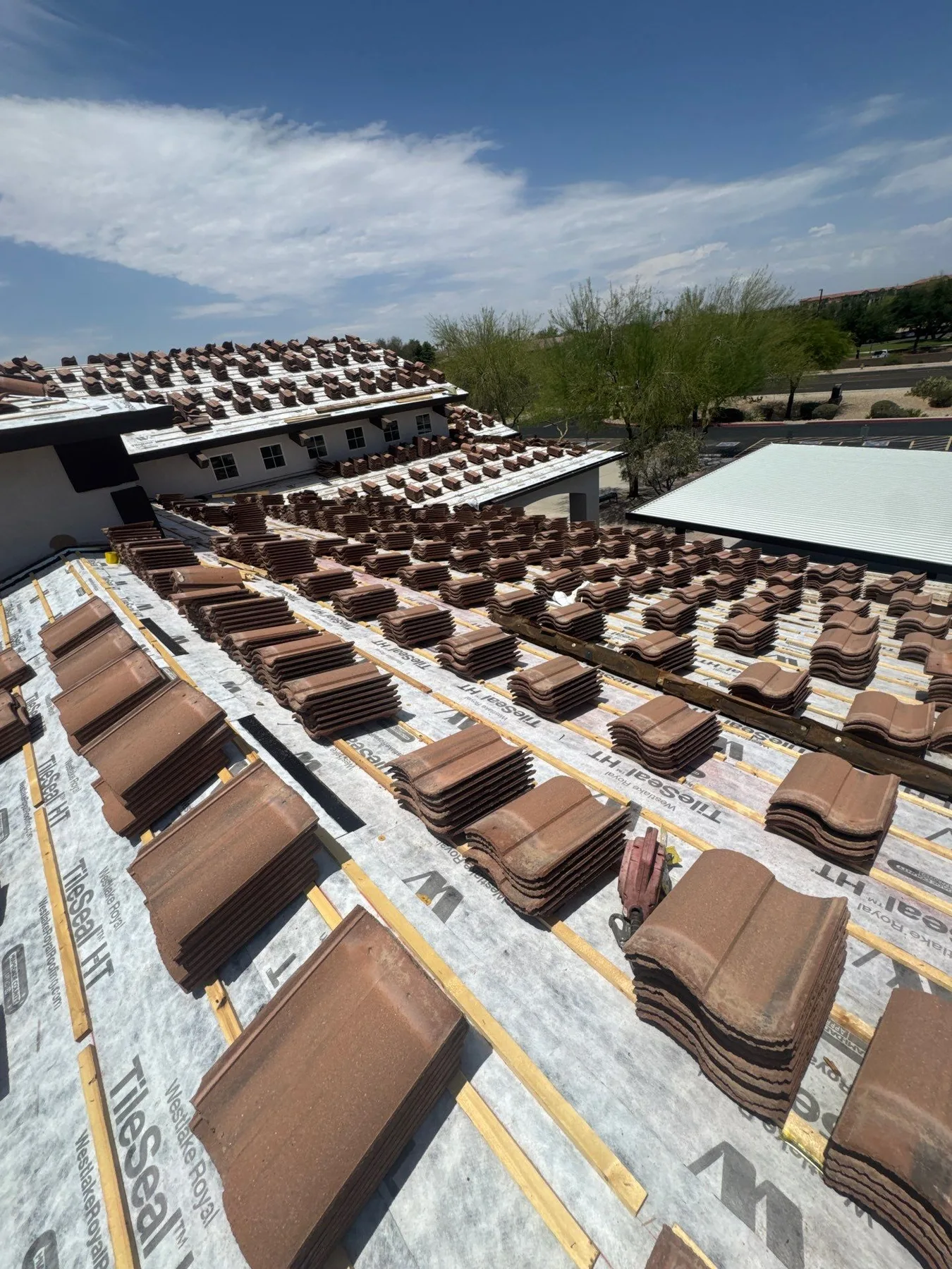 Low-angle rooftop view of silver underlayment lined with stacked brown tiles and battens