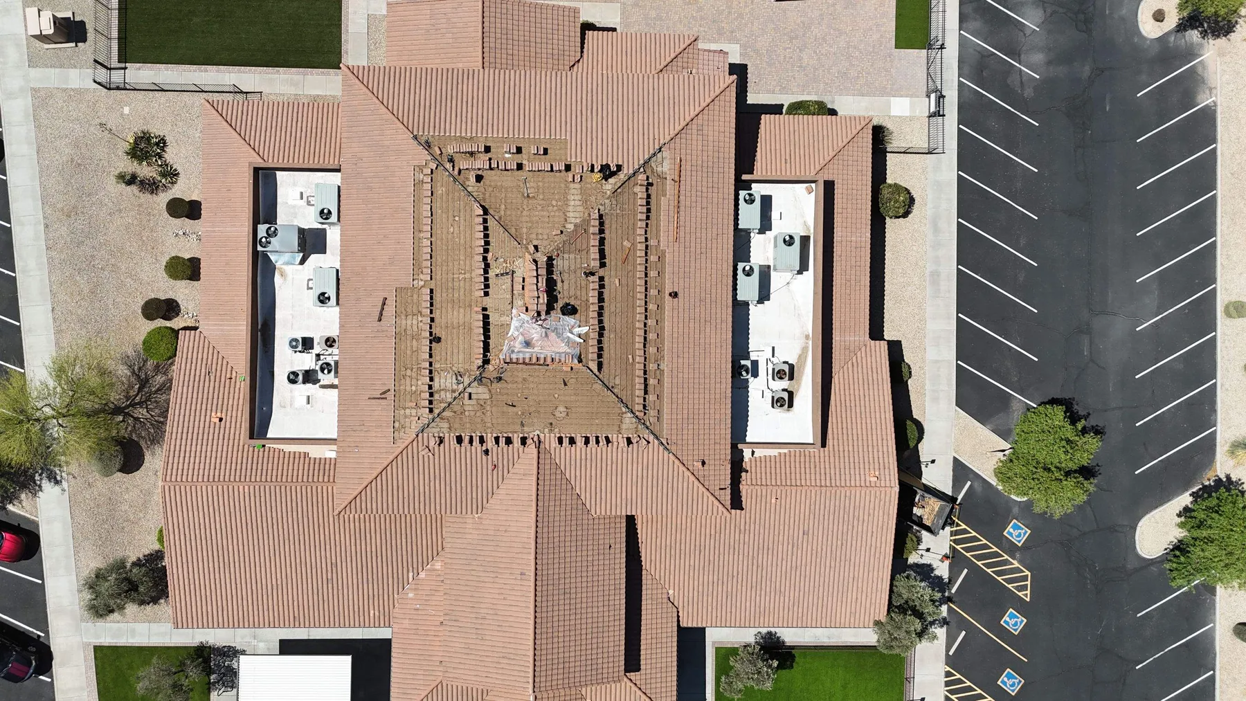 Top-down aerial view of completed tan tile roof with two white mechanical wells beside parking