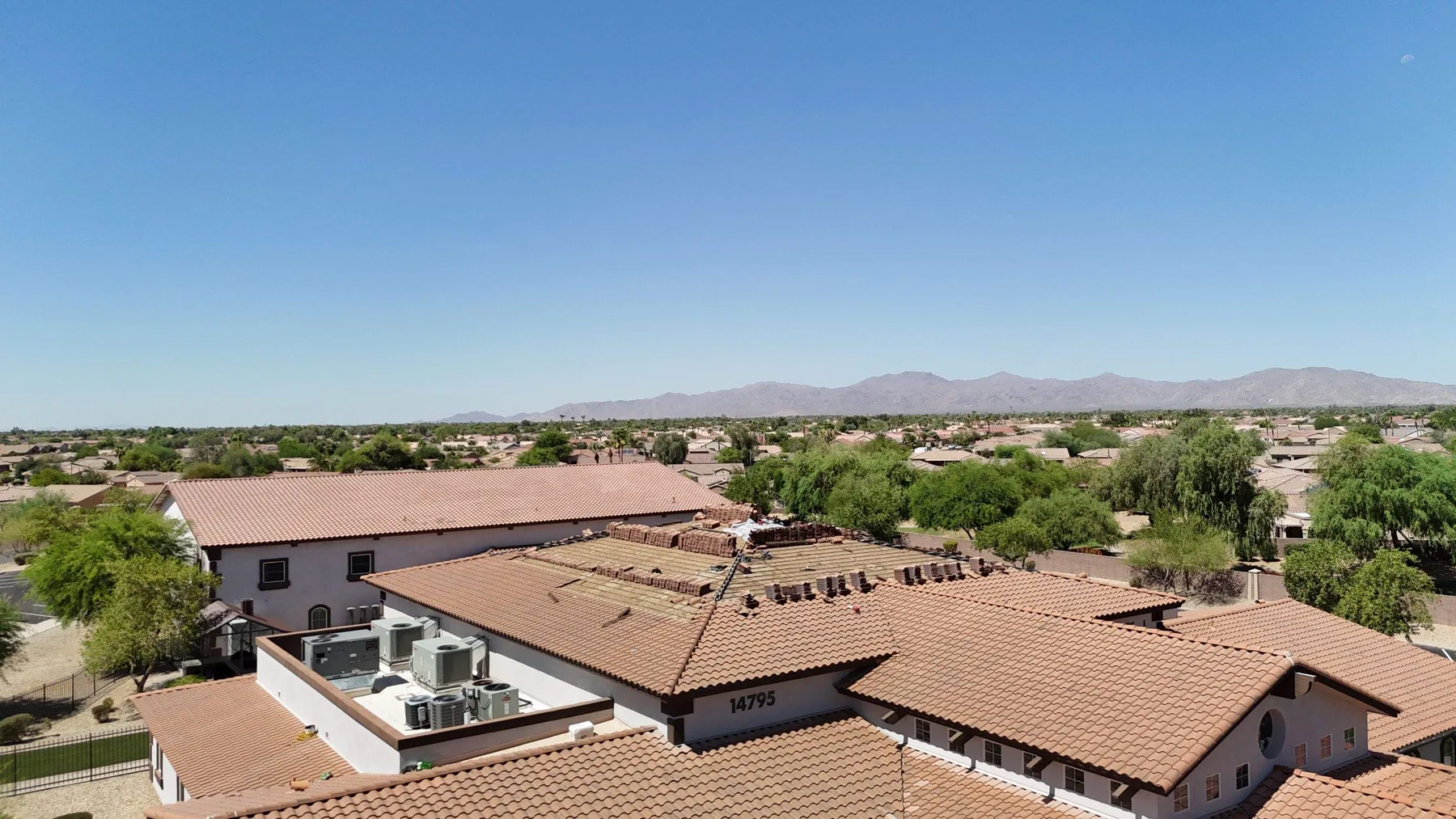 Elevated panoramic view of completed reddish-brown tile roofs against desert neighborhood and mountains