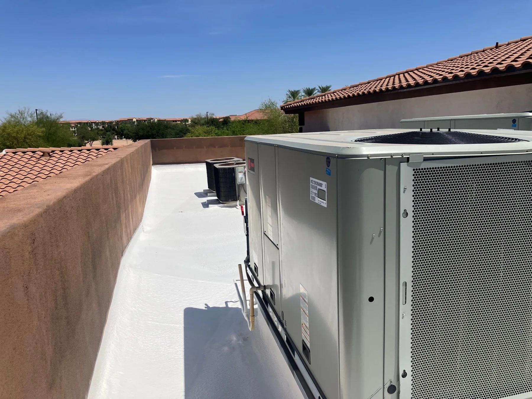 Rooftop-level view of bright white coated flat roof beside large gray HVAC equipment