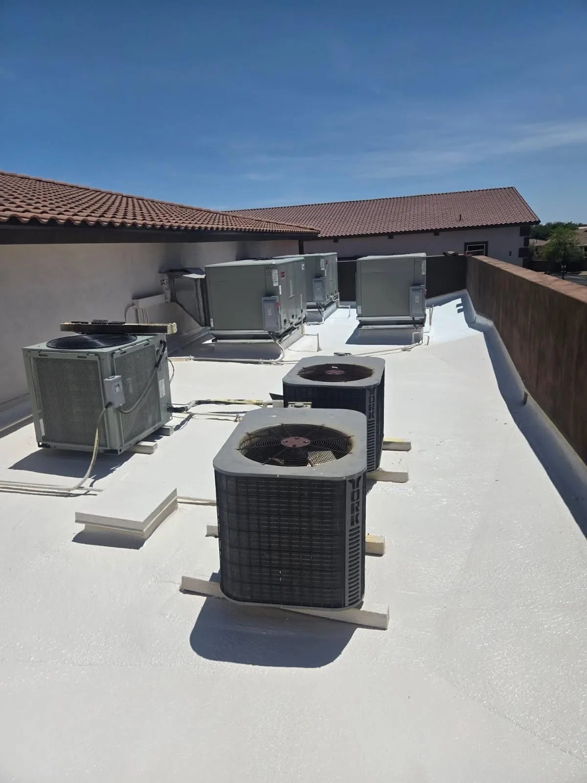 Low rooftop view of white coated flat surface with several gray cooling units