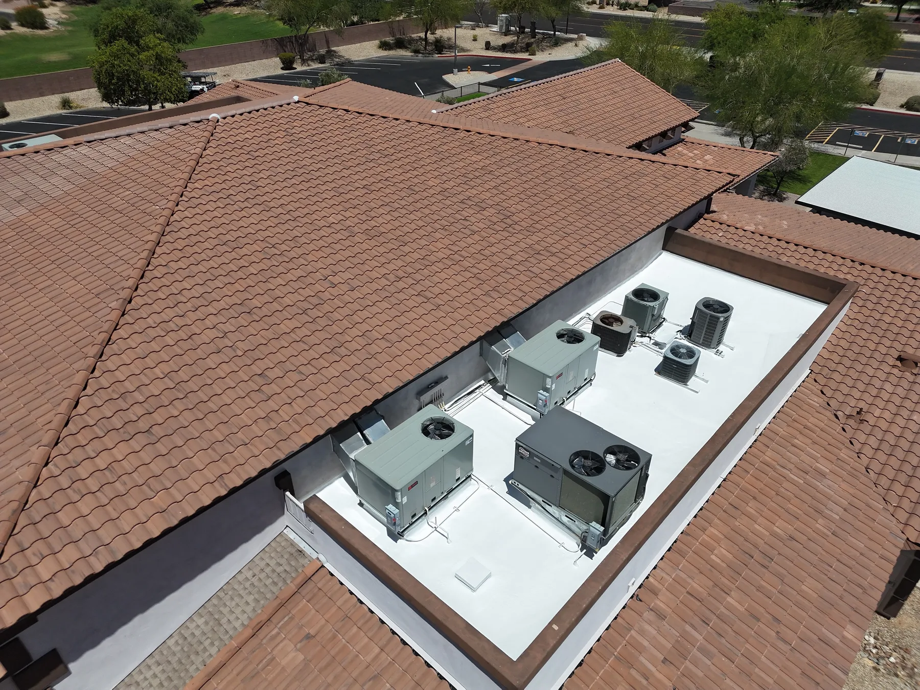Oblique aerial view of white coated equipment roof recessed within broad reddish tile slopes