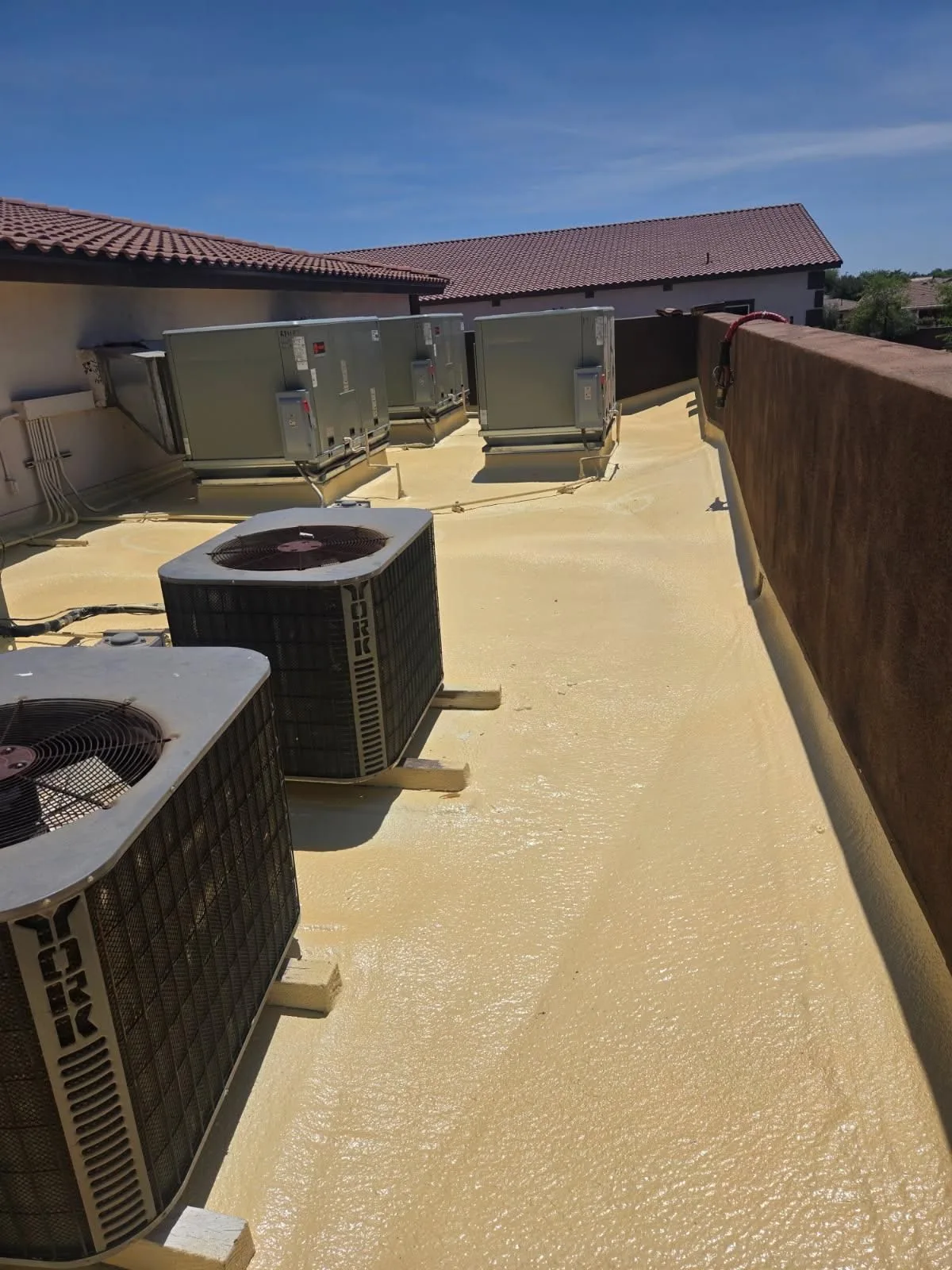 Rooftop-level view of tan coated flat roof with cooling units between brown parapets