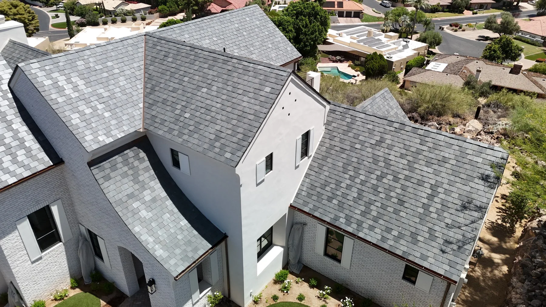 Oblique aerial view of gray slate-style roofing across intersecting gables and curved entry canopy