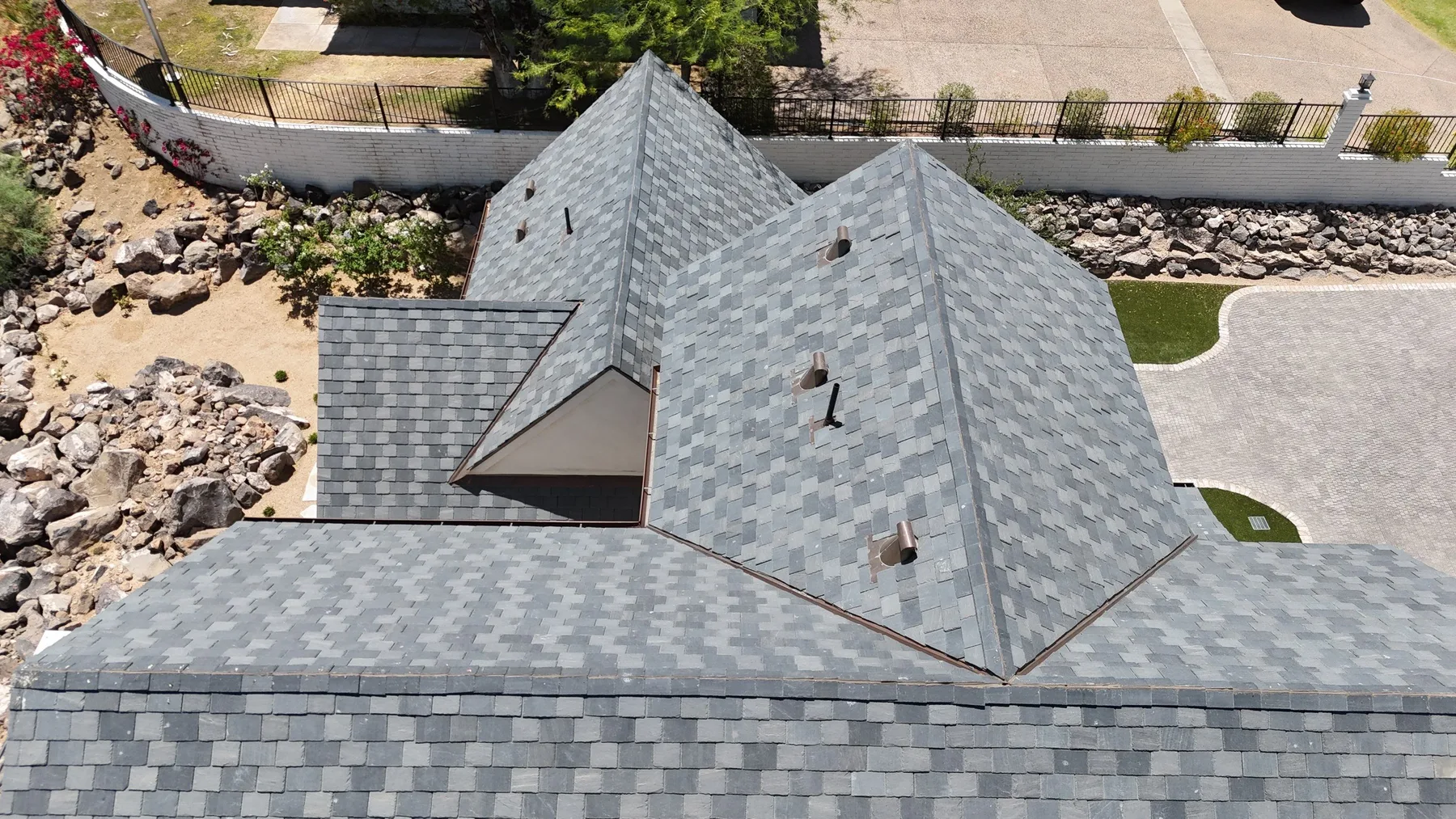 Near-overhead view of variegated gray slate-style hips, valleys, and several pipe vents
