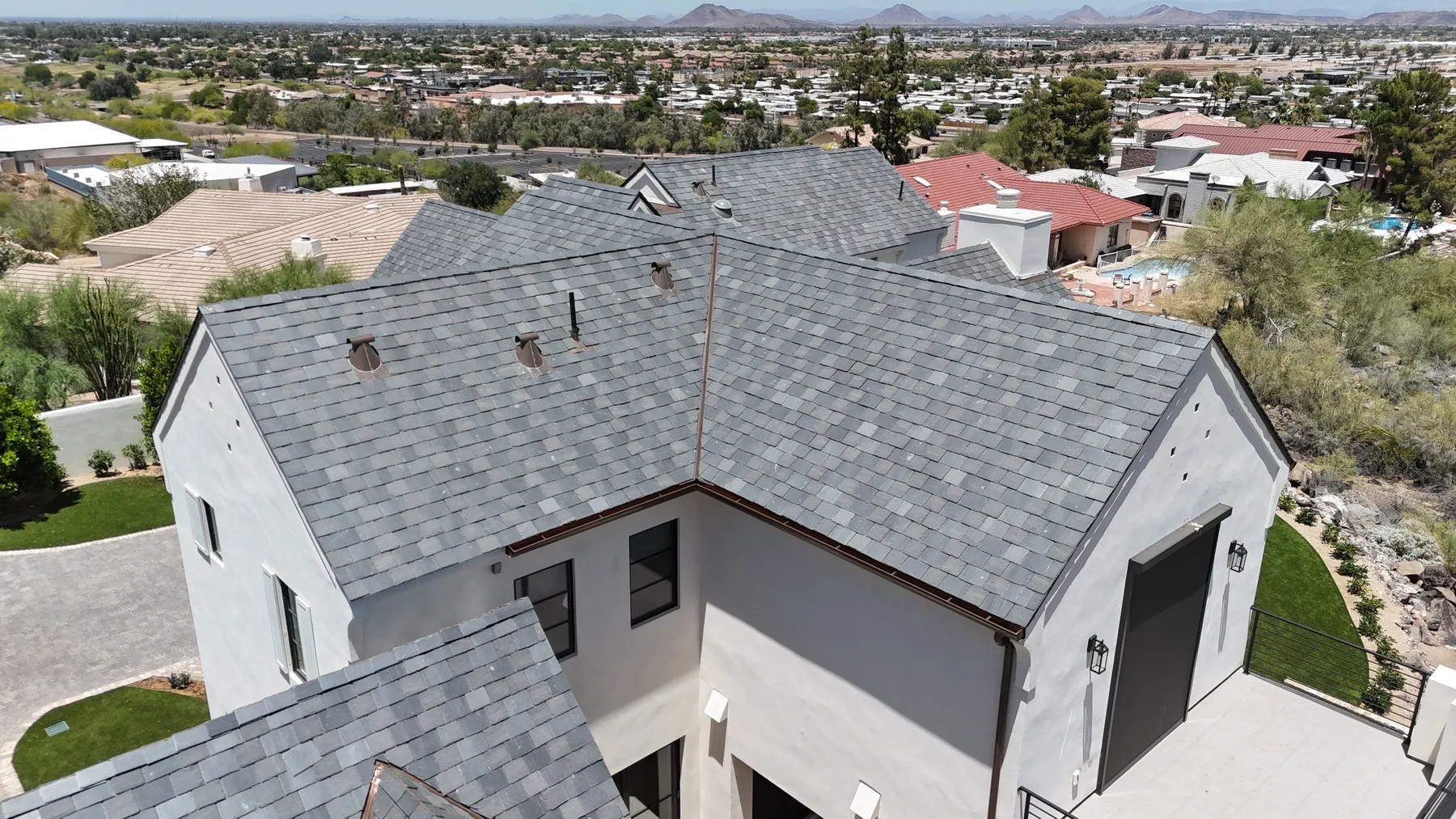 Rear oblique aerial view of gray slate-style roofing with intersecting hips and multiple gable ends