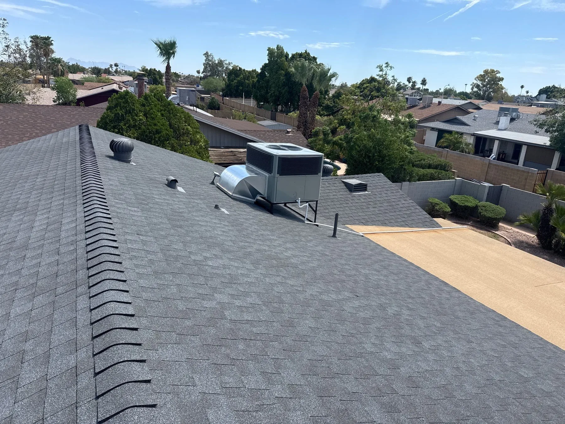 Rooftop perspective across gray shingles with ridge caps, pipe vents, and cooling equipment