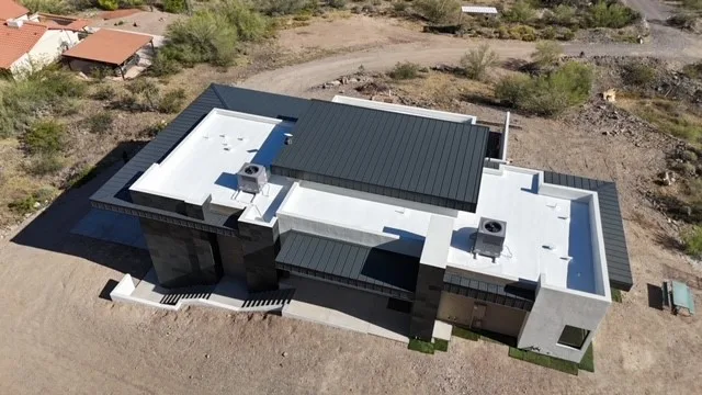 Oblique aerial view of dark ribbed metal roofing beside white flat sections and rooftop units