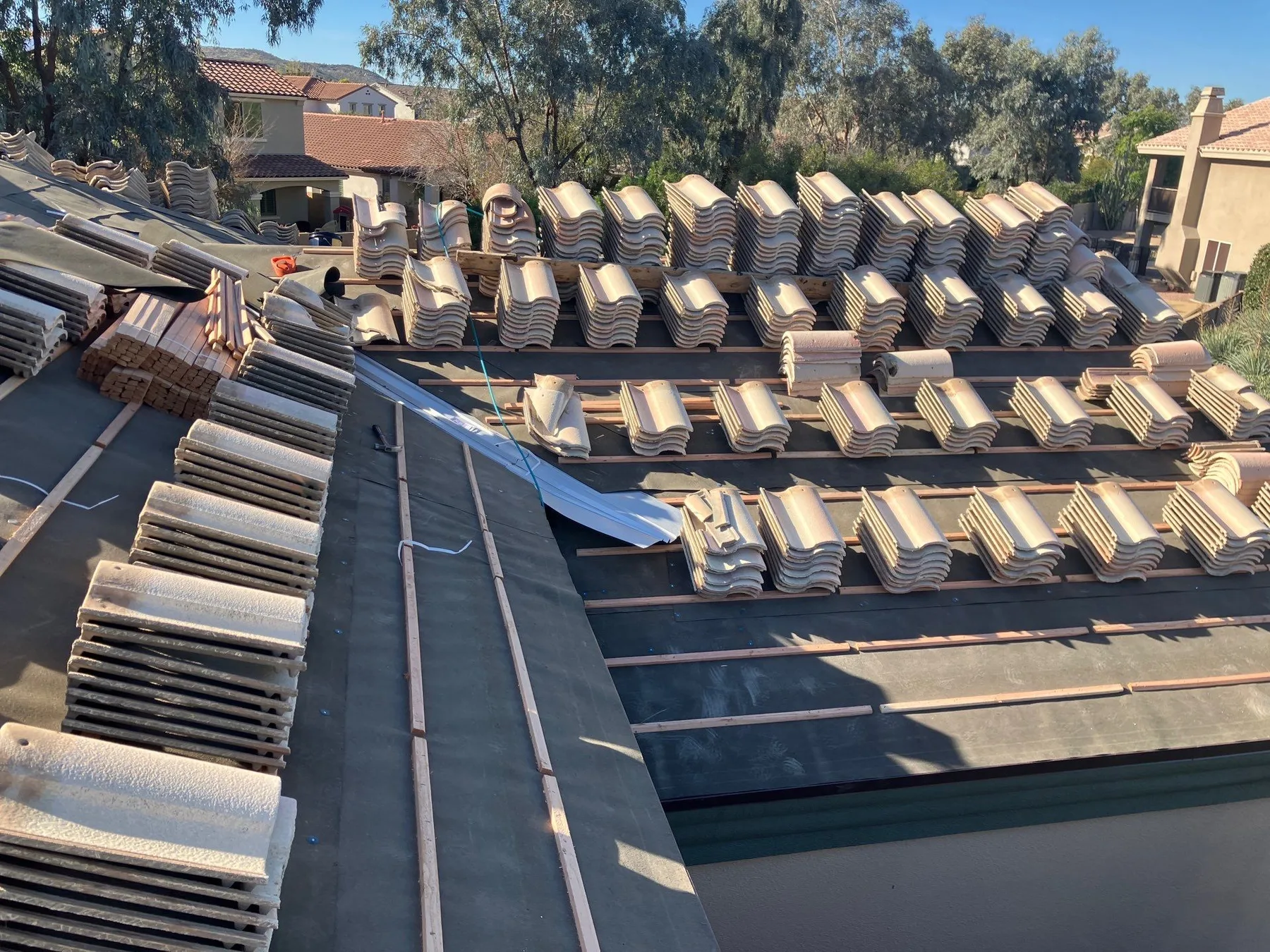 Elevated view of partially tiled roof with tan bundles arranged over black underlayment