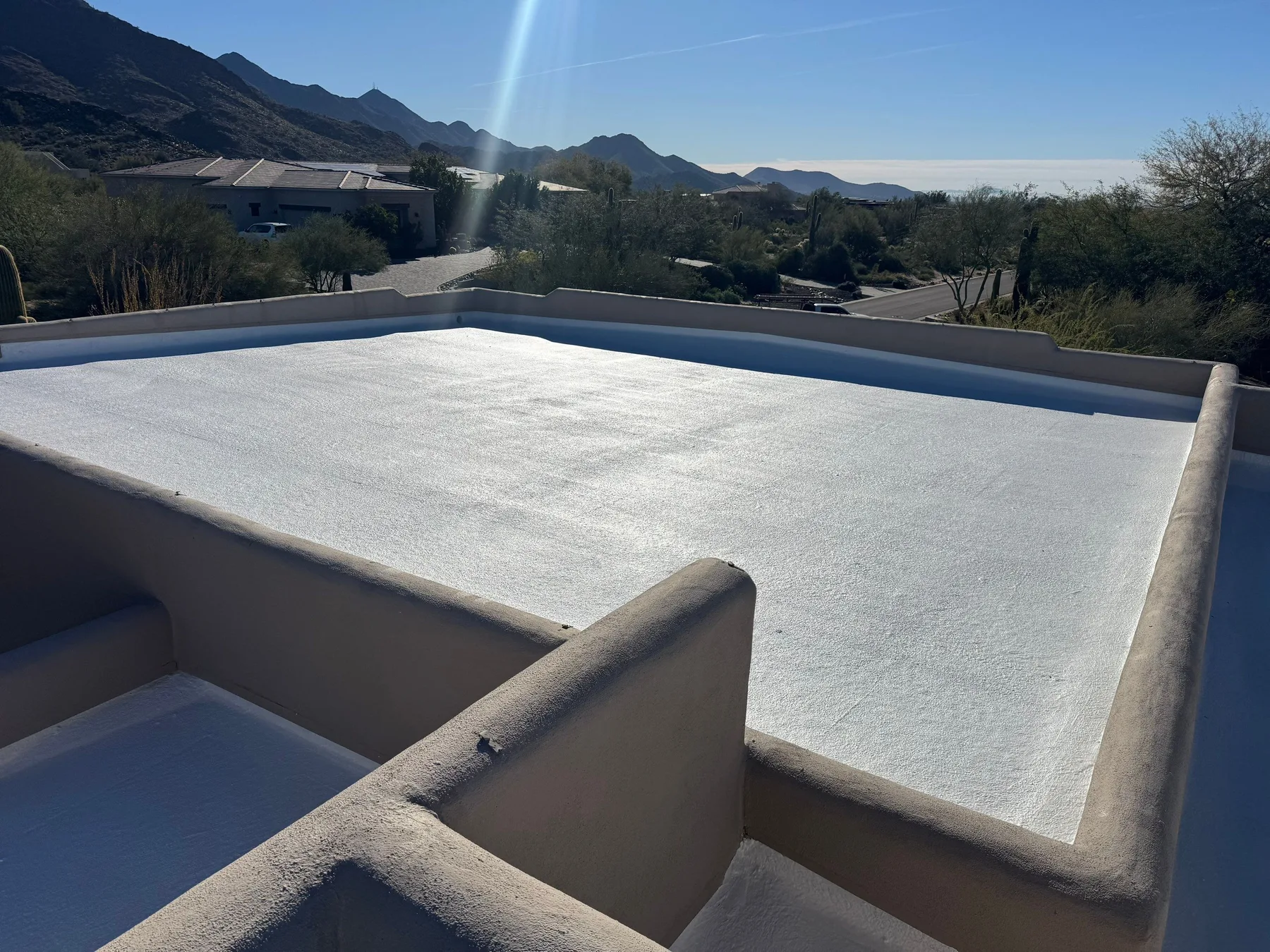 Rooftop view of smooth white flat roofing bordered by rounded gray parapet walls