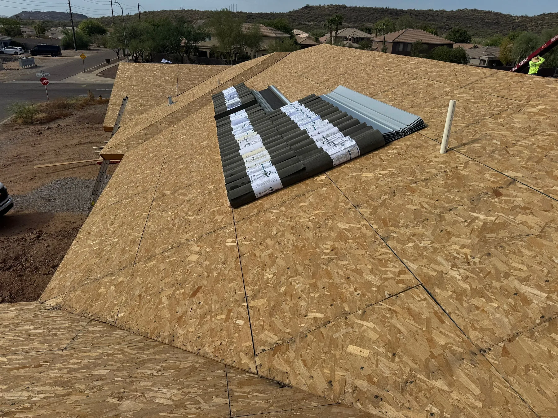 Elevated view of bare wood roof decking with packaged tiles stacked near the ridge
