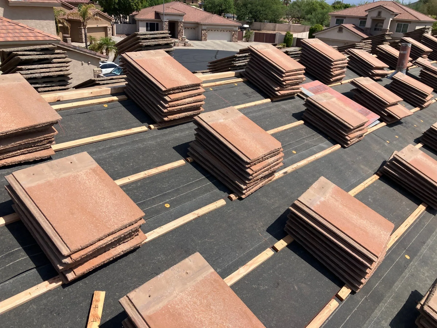 Rooftop view of red square tile stacks spaced across black underlayment and battens
