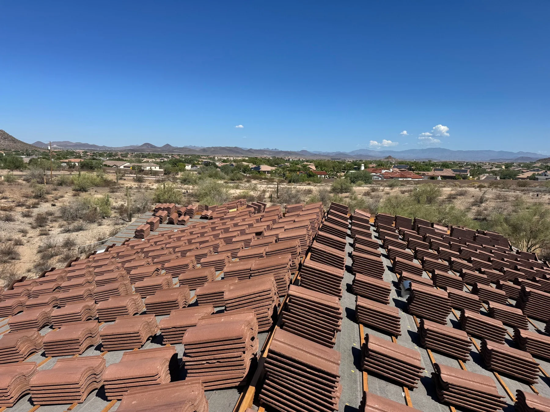 Rooftop view of reddish tile stacks lining ridges over black underlayment and battens