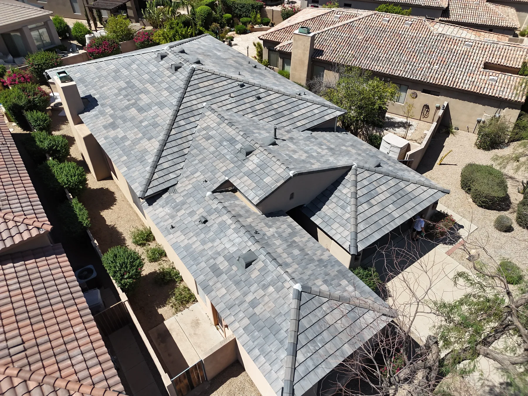 Aerial view of completed variegated gray tile roof with chimney and intersecting hips