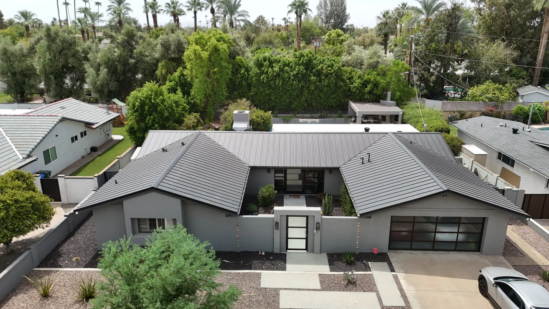 Frontal aerial view of completed dark gray metal hip roofs around a recessed entry
