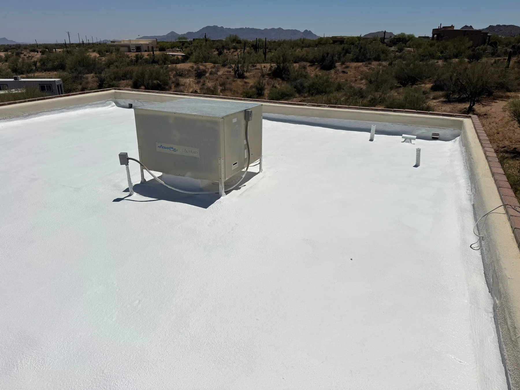 Rooftop view of smooth white flat roofing with central HVAC unit and vent pipes