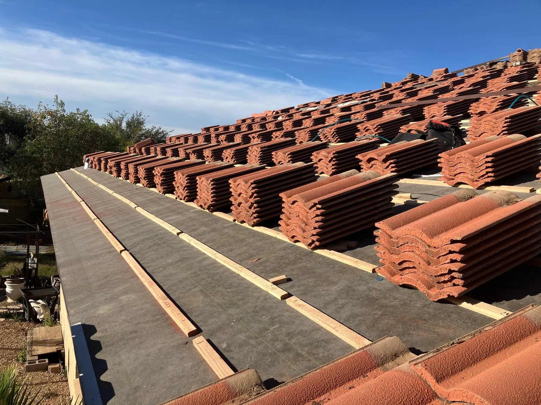 Roof-level view of reddish tiles stacked beside exposed battens and dark underlayment