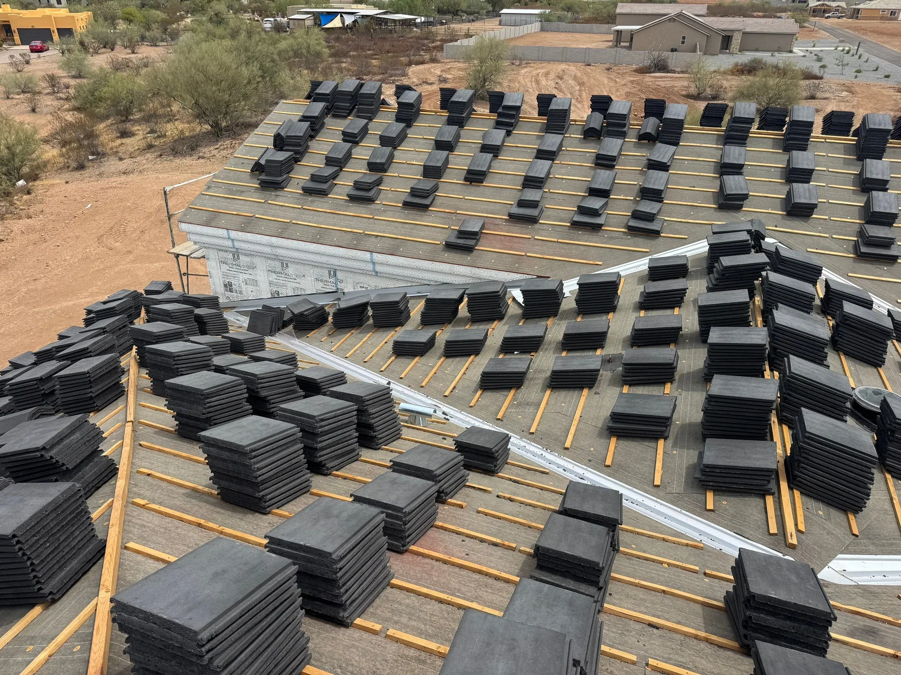 Oblique rooftop view of dark tile stacks across gray underlayment and yellow battens