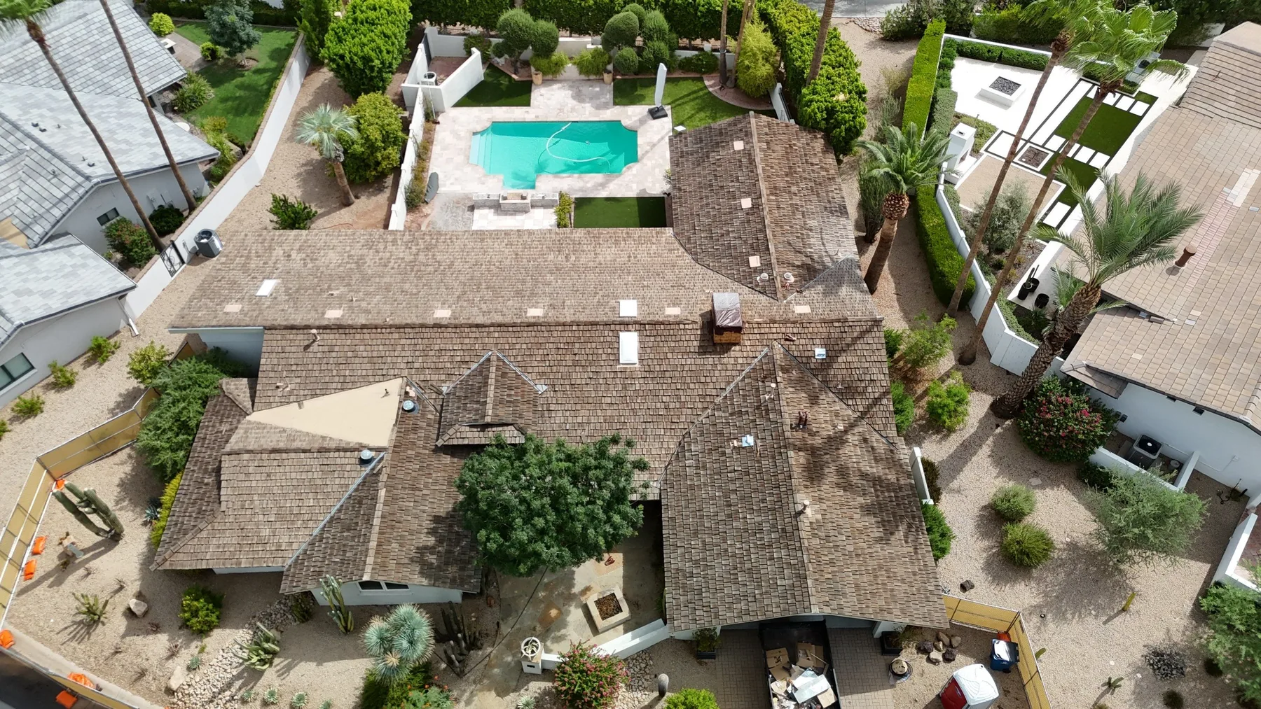 Top-down aerial view of brown shingle roof with complex hips and central tree canopy