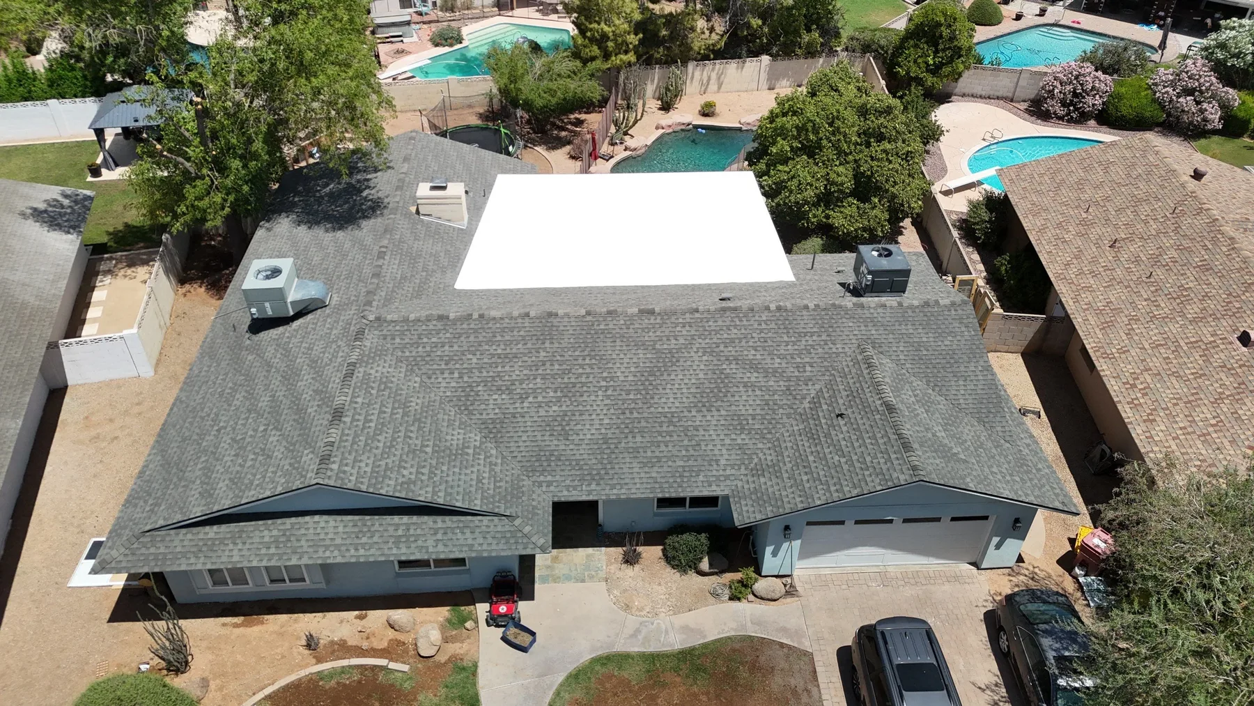 Oblique aerial view of gray shingle roof surrounding a bright white flat-roof section