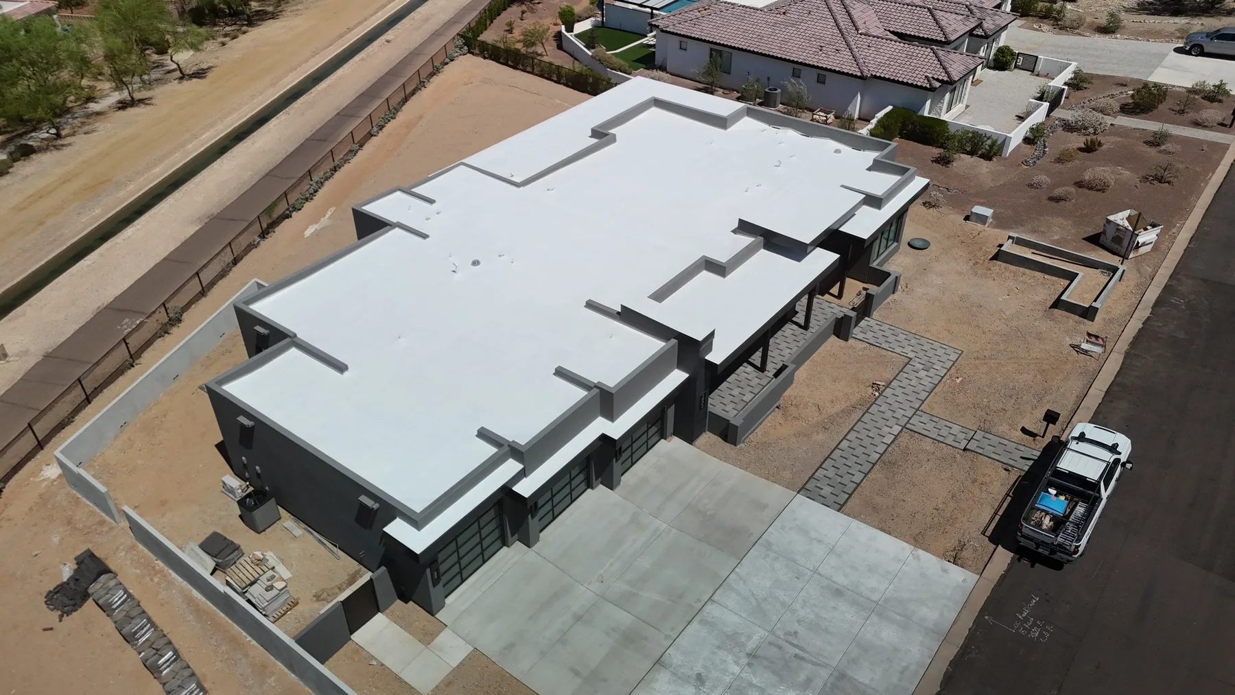 High oblique aerial view of light-gray flat roofing with stepped parapets and covered entry