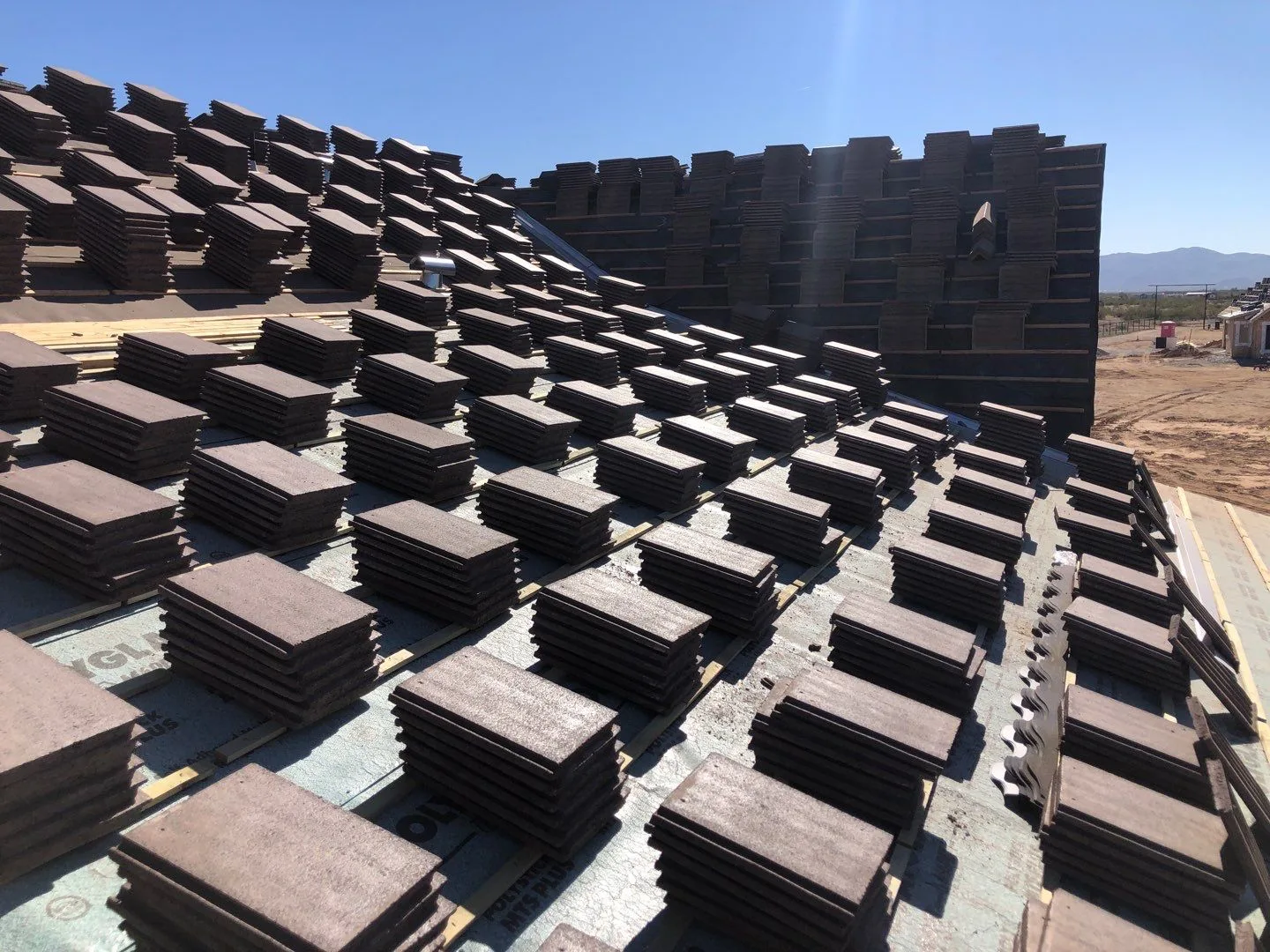 Low-angle rooftop view of dark brown tile stacks beside intersecting slopes and upright pallets
