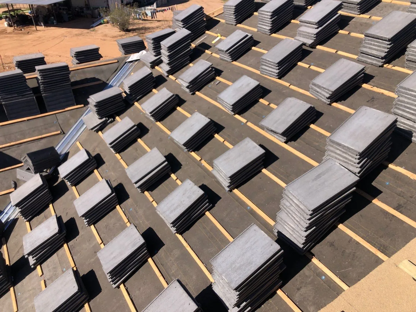 Overhead close view of gray tile stacks spaced across black underlayment and tan battens