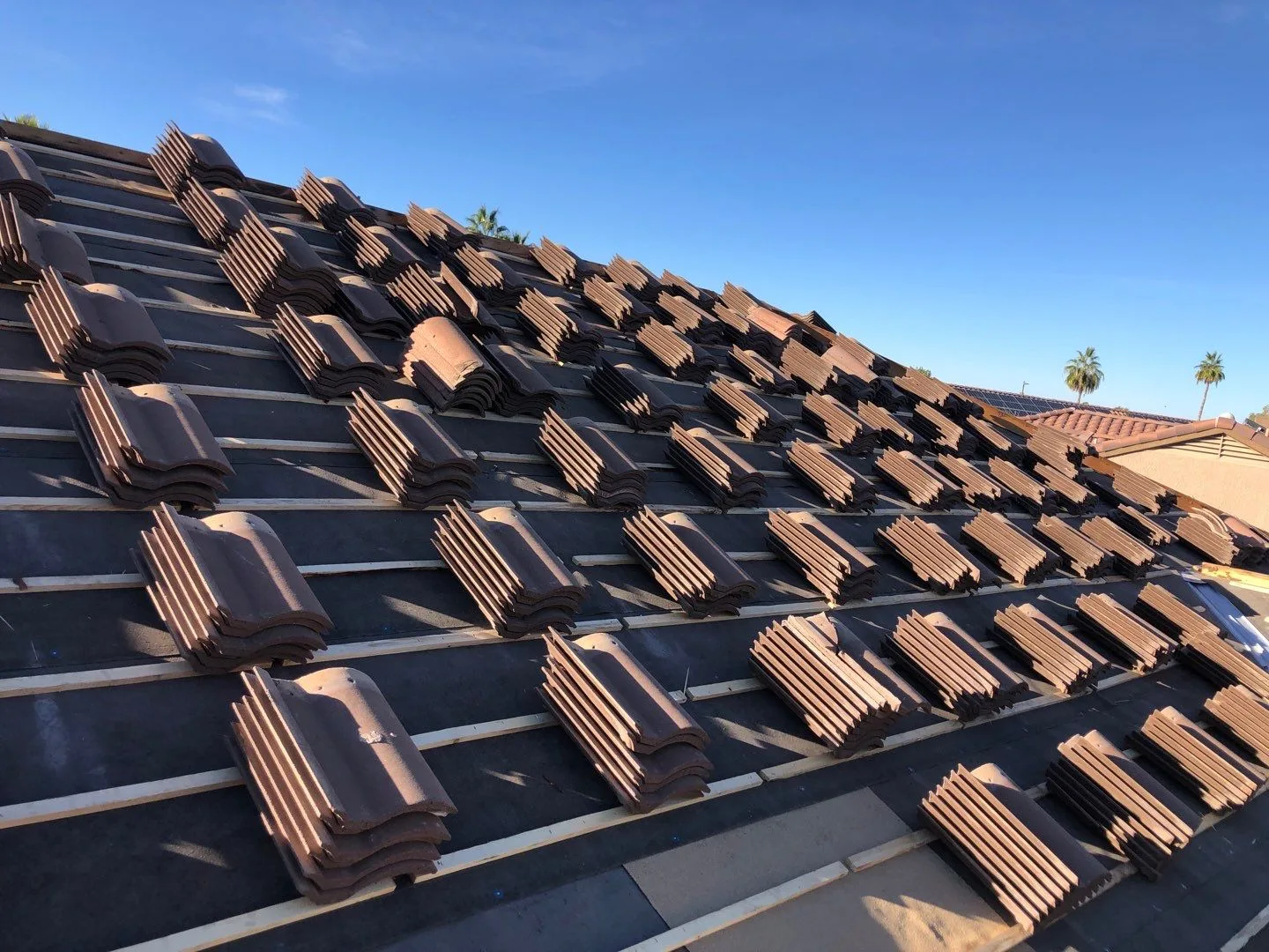 Low-angle roof view of bundled brown tiles spaced across dark underlayment and battens