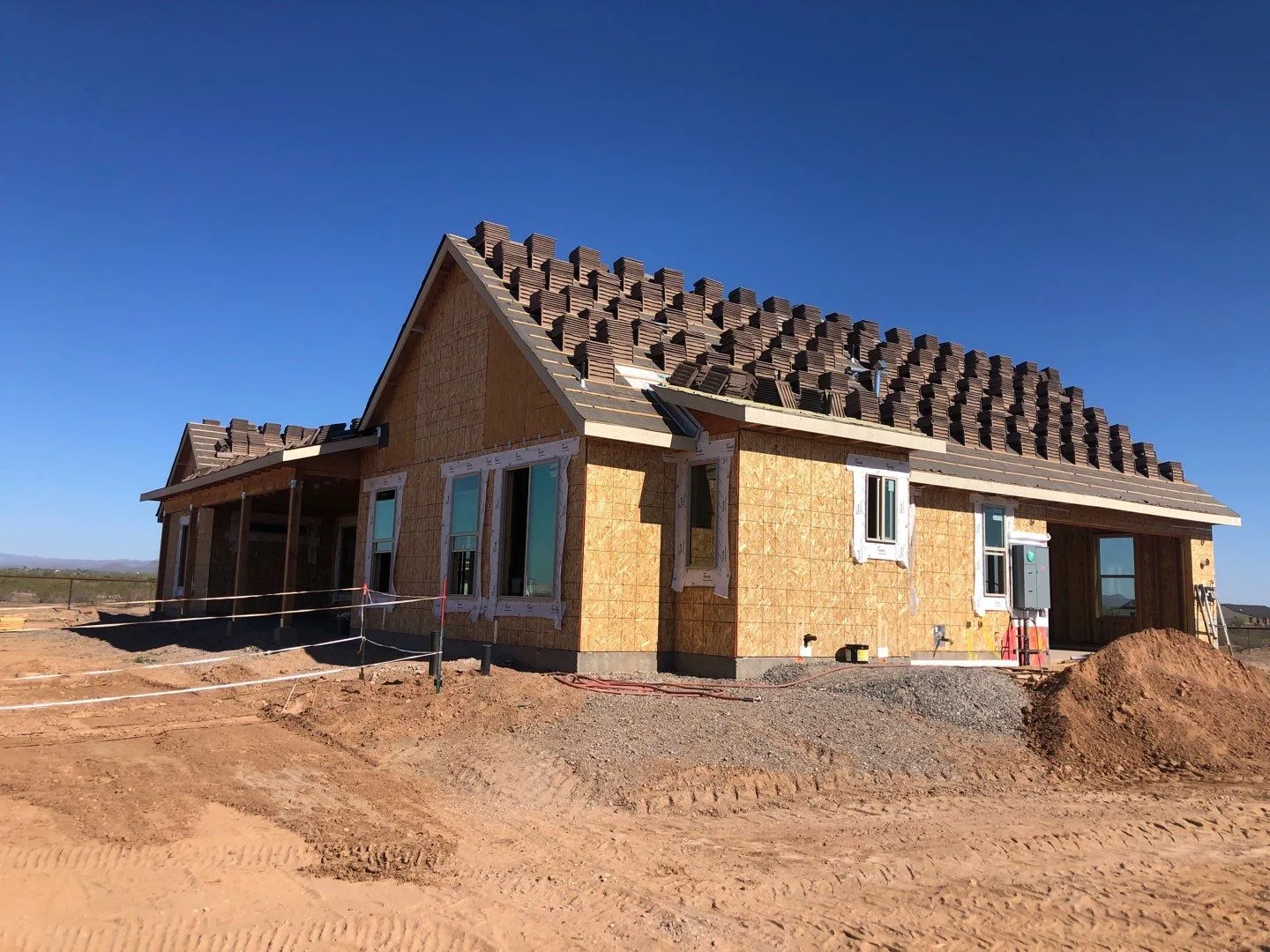 Ground-level view of partially tiled brown roof over exposed wood wall sheathing