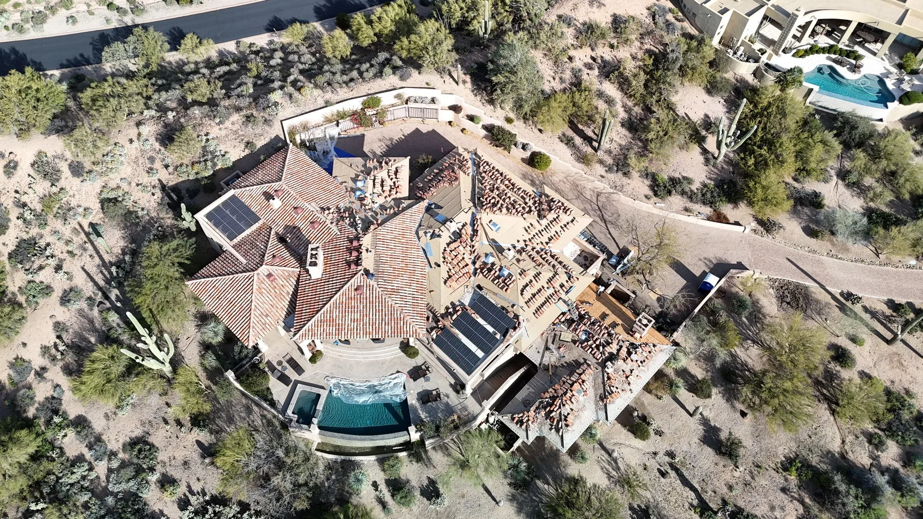 Top-down aerial view of partially tiled reddish roof surrounding a curved swimming pool