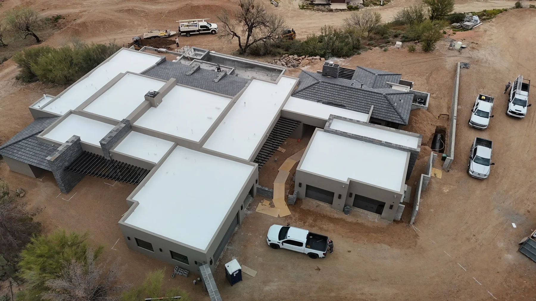 Aerial view of white low-slope roofs adjoining gray tiled sections beside parked vehicles