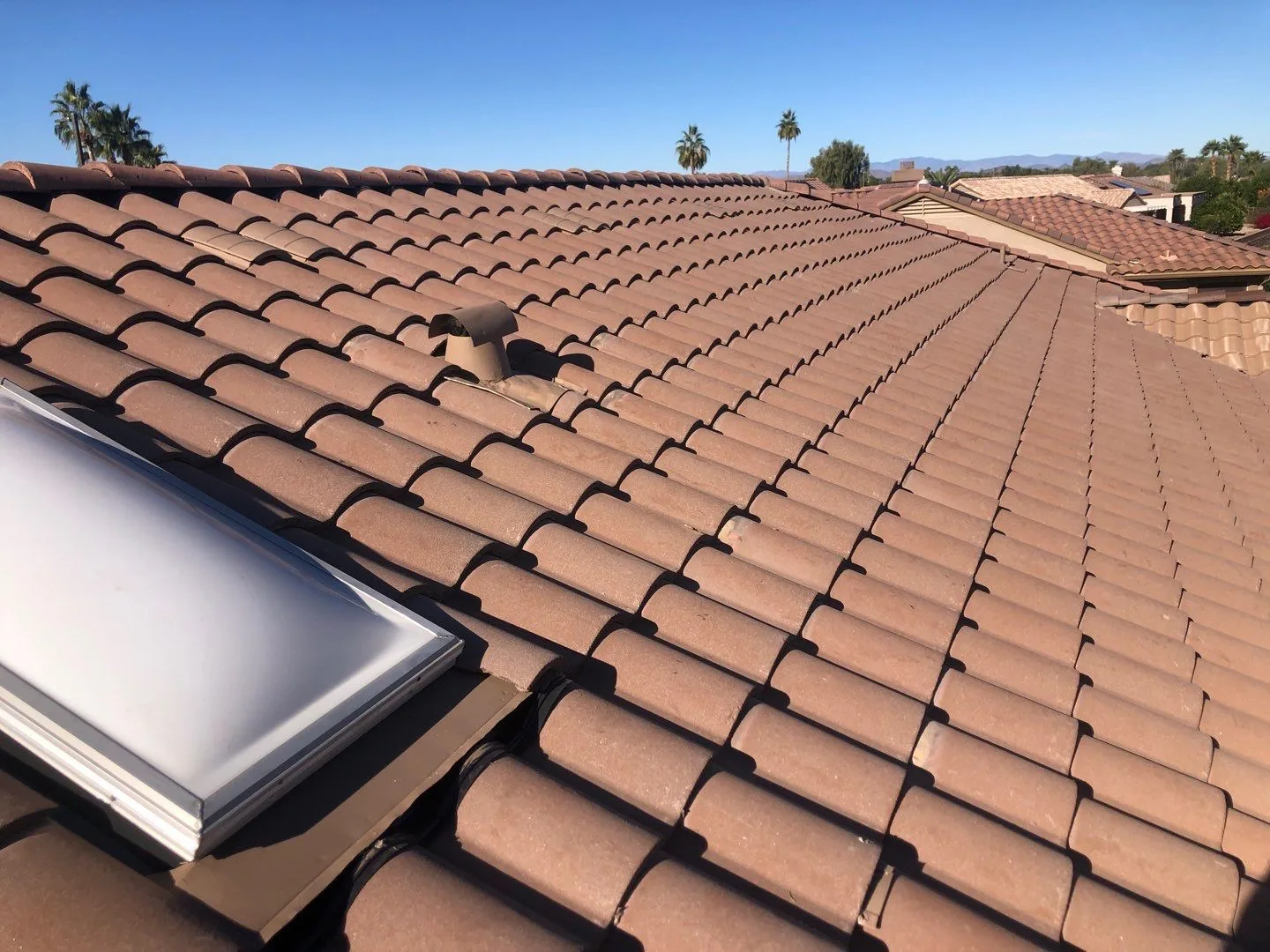 Roof-level view across completed terracotta-colored tiles with a projecting rectangular skylight