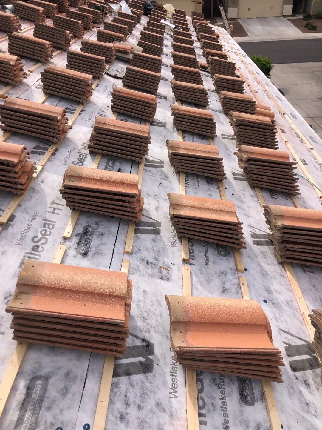 Close overhead view of terracotta-colored tile bundles arranged on white underlayment and battens