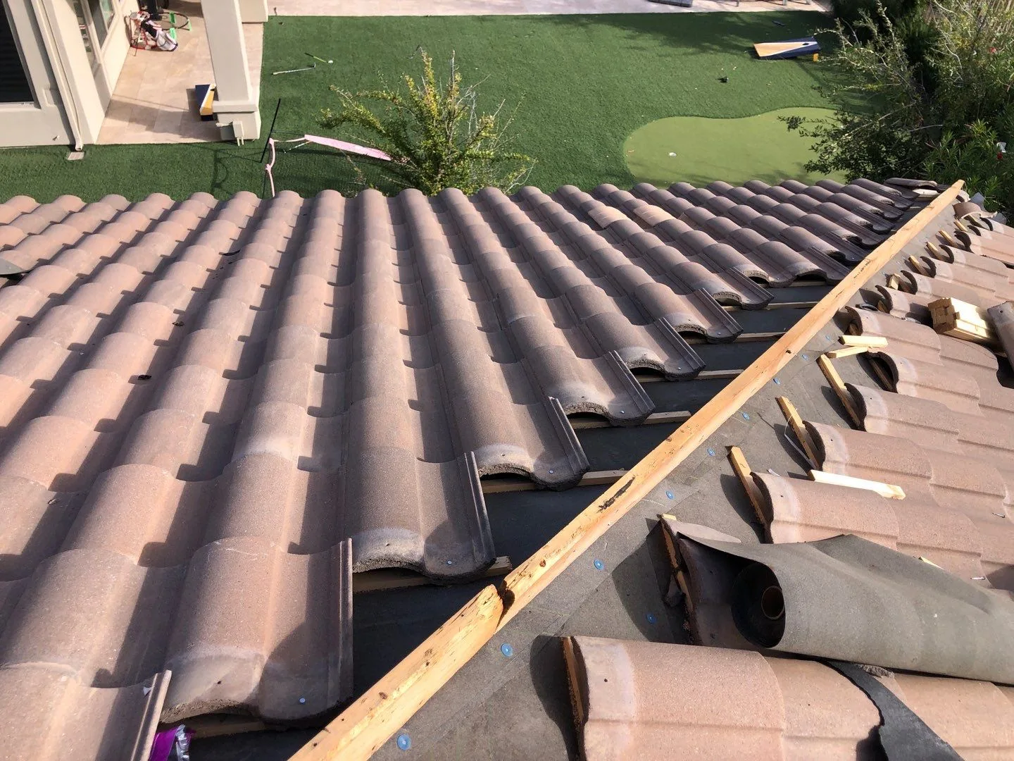 Close oblique view of brown curved tiles partly installed over dark underlayment