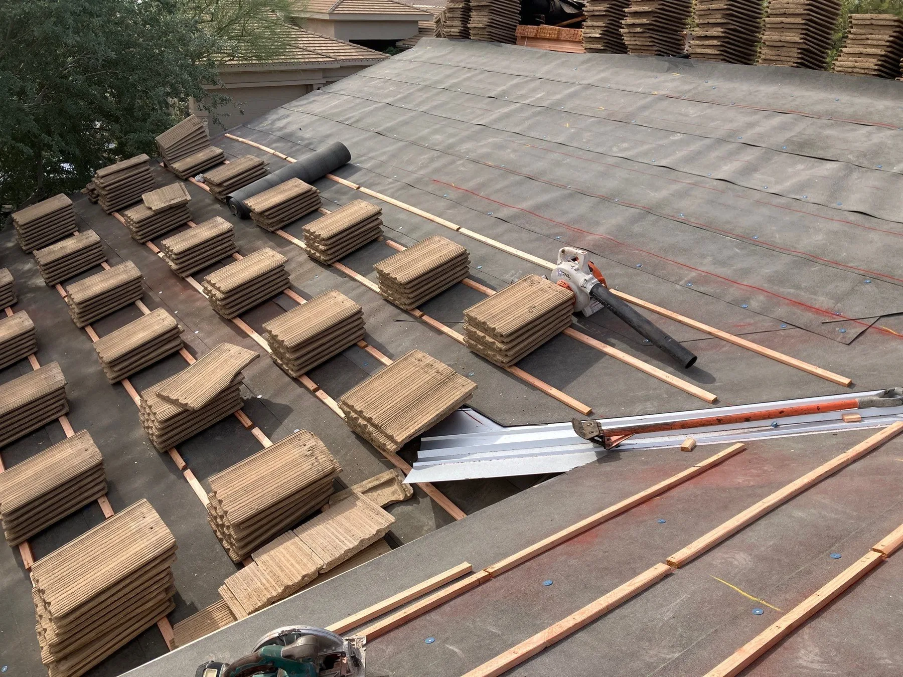 Elevated view of stacked brown flat tiles arranged across dark underlayment and battens