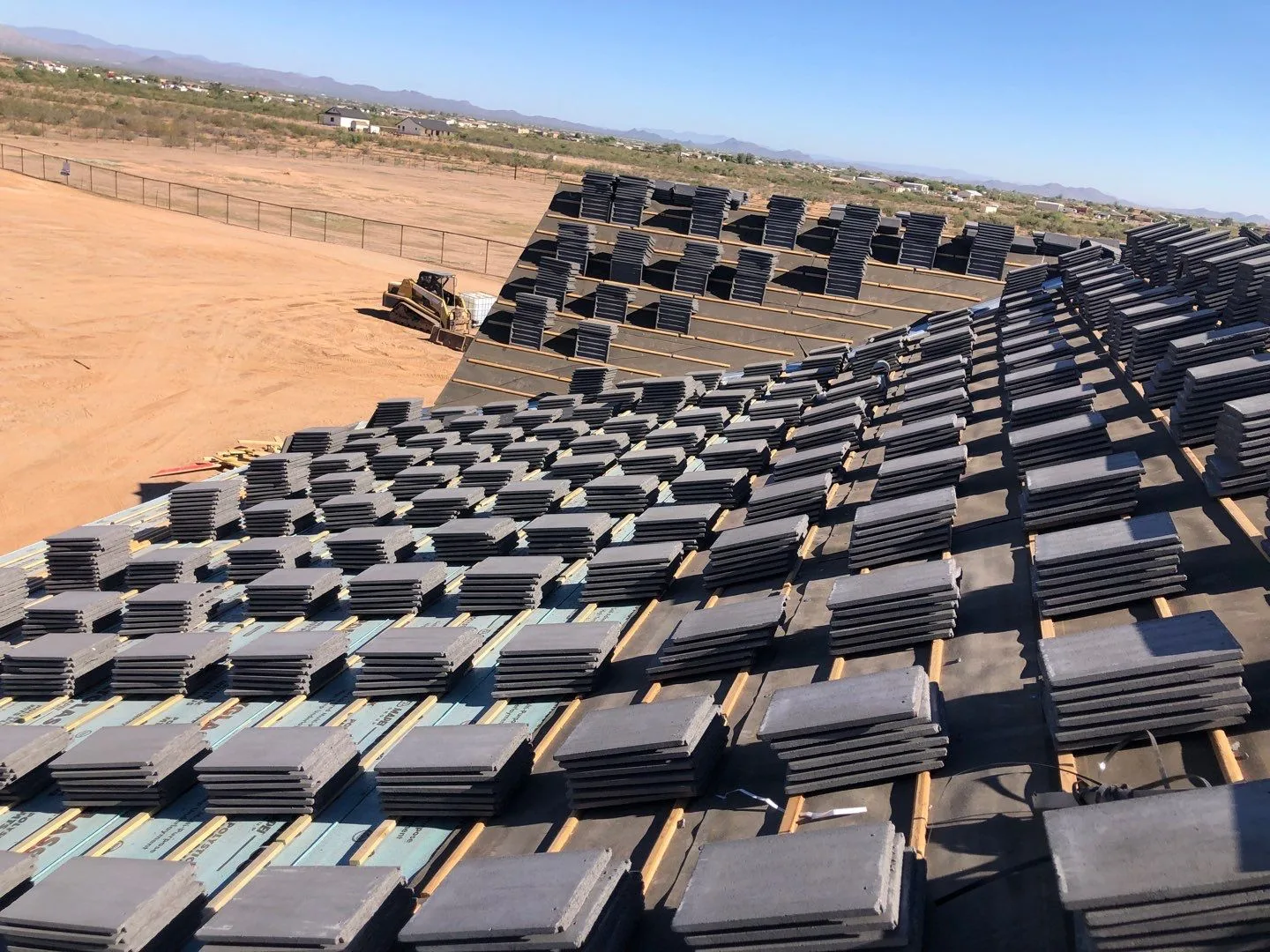 Steep rooftop view of dark gray flat tiles staged in rows over underlayment