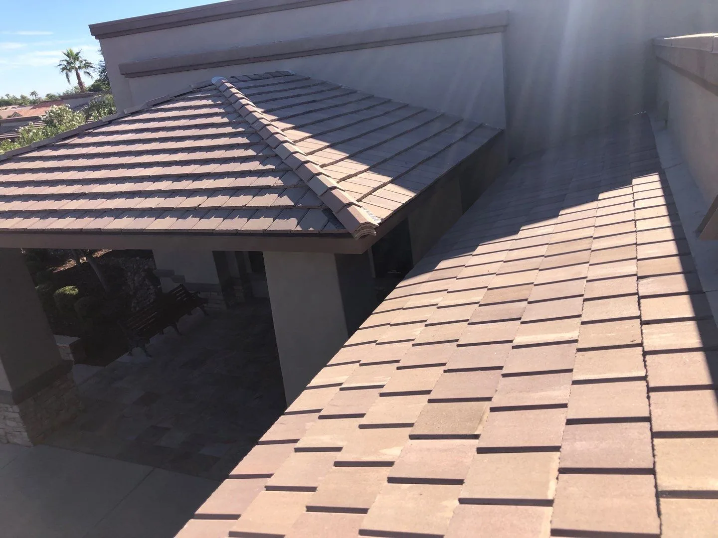 Close rooftop view of tan flat tiles meeting intersecting slopes beneath a stucco wall