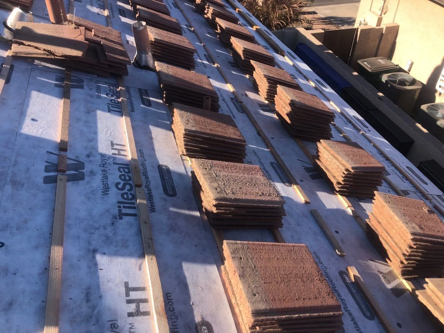 Oblique rooftop view of reddish flat tile stacks on gray underlayment between wooden battens