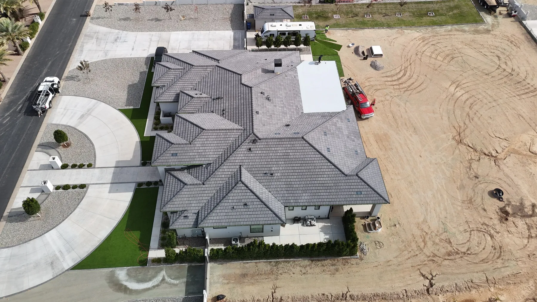 Top-down aerial view of gray tiled gables adjoining a white low-slope roof and circular driveway