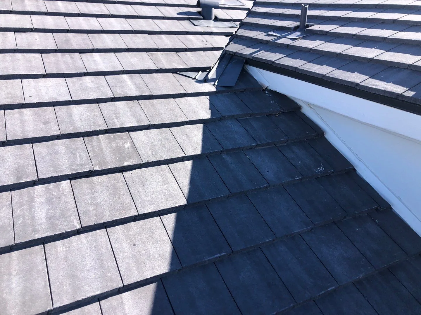 Close view of completed dark gray flat tiles beside white walls and black valley flashing