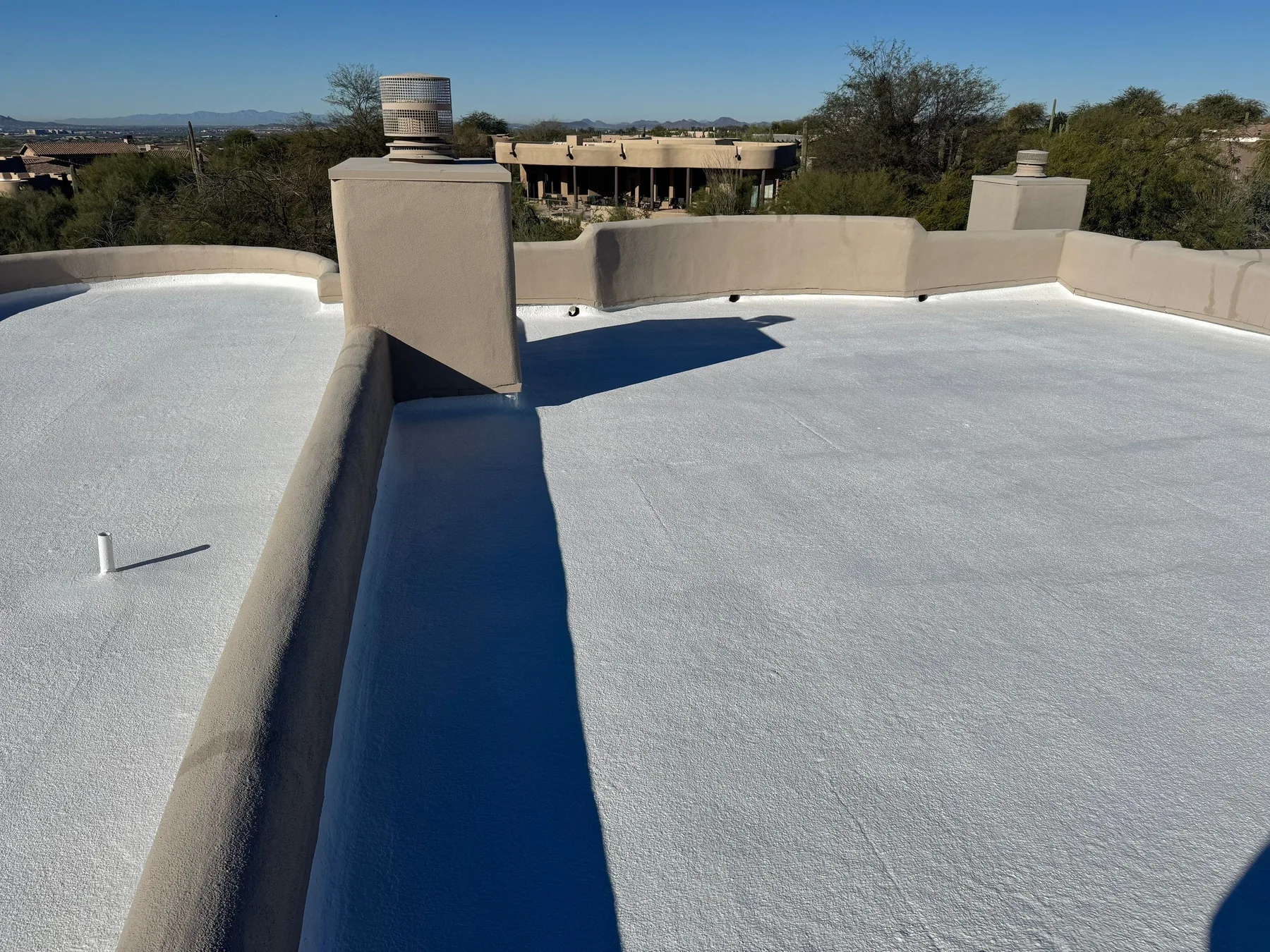 Rooftop perspective of light gray flat covering bounded by beige parapets and a chimney