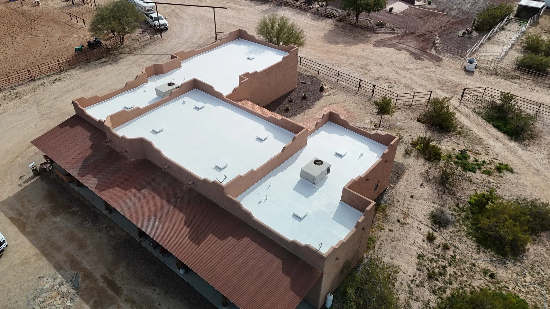 Oblique aerial view of white flat roof sections bordered by reddish-brown low-slope panels
