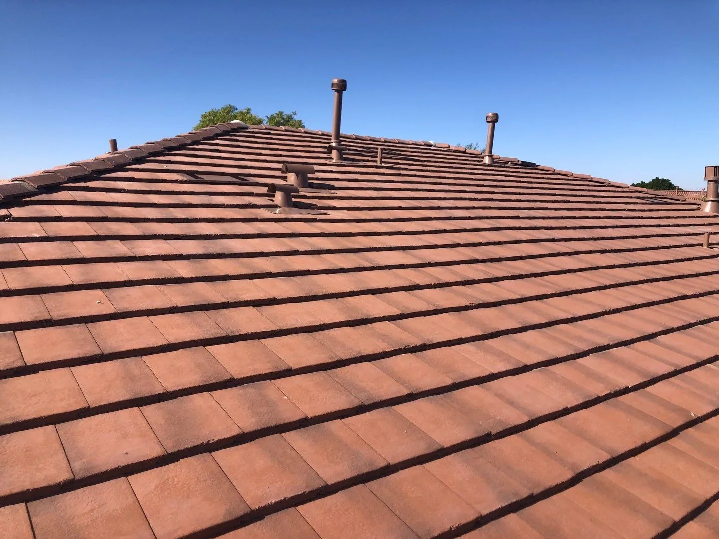 Low-angle rooftop view of completed reddish-brown tiles with several vent pipes